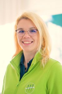 Sabrina Sierks, Produktmanagerin für den Akupaix Onlineshop für Akupunktur-, Heilpraktiker- und TCM-Bedarf. Die blonde junge Frau mit Brille und einem hellgrünen Praxis-Shirt lächelt freundlich in die Kamera.